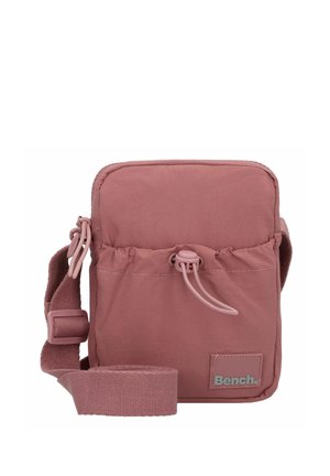 Kompakte rosa Tasche aus weichem Stoff, mit einfachem Design, verstellbarem Tragegurt, Kordelzugverschluss und einem kleinen Logo-Patch.