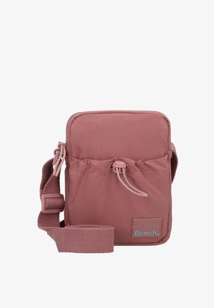 Compact pink bag made of soft fabric, featuring a simple design, adjustable strap, drawstring closure, and a small logo patch.