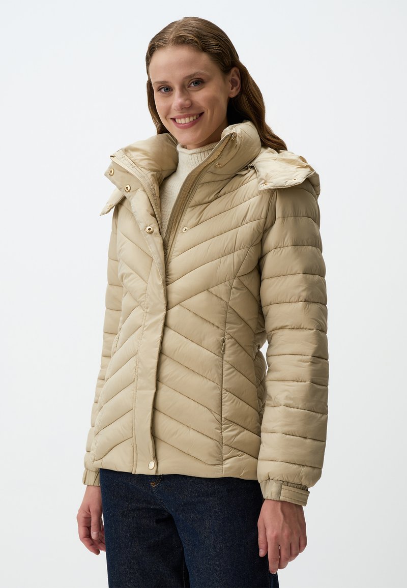 Beige pufferjack met diagonale stikseling, een hoge kraag en drukknoopjes, met elastische manchetten en een gladde, glanzende textuur.