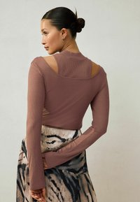 Długi rękaw, prążkowany top w kolorze mauve z designem otwartych ramion. Połączony z nadrukowaną spódnicą w odcieniach beżu i czerni.