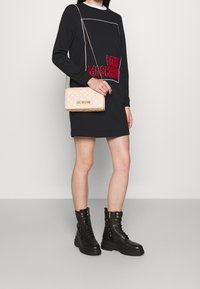 Black long-sleeve dress with white outline and red embroidered "LOVE MOSCHINO" logo. Paired with chunky black lace-up boots and beige quilted handbag.