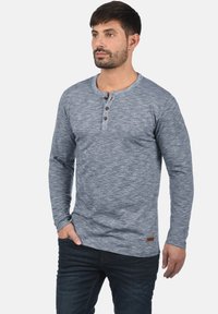 Hosszú ujjú henley póló heather szürke anyagból, kerek nyakkivágással, három gombos záródással és egy kis logóval a szegélyén.