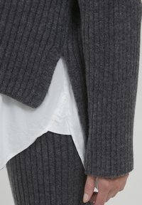 Gray ribbed knit sweater with a split hem, layered over a white shirt. Textured wool blend fabric and fitted sleeves are visible.