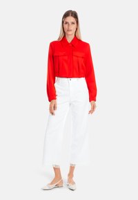Red cropped blouse with a collar and two front pockets, paired with white wide-leg pants featuring lace trim at the hem. Neutral shoes complete the look.