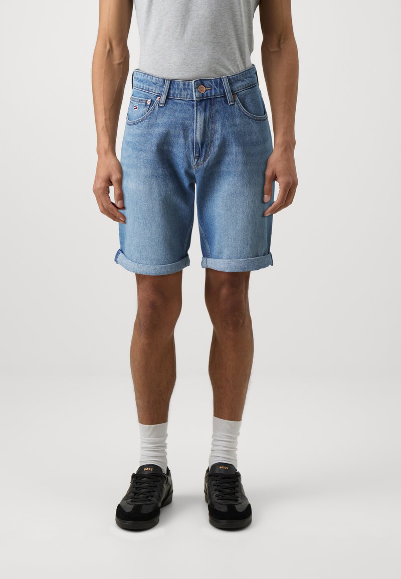 Lyseblå denimshorts med oppbrett, fem lommer, og glidelås, kombinert med en grå t-skjorte og svarte joggesko.