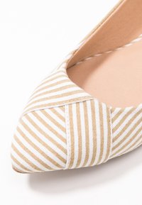 Randig platt sko med beige och vit canvasmaterial, spetsig tådesign och en slät innersula, med synliga sömnadsdetaljer.