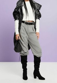 Giacca a vento nera, maglione bianco a coste, pantaloni grigi plissettati, stivali alti con tacco neri e borsa nera in paillettes.