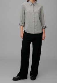 Grijze, lange mouwen blouse met een puntige kraag, één borstzak en opgerolde mouwen, gecombineerd met brede zwarte broeken en zwarte laarzen.