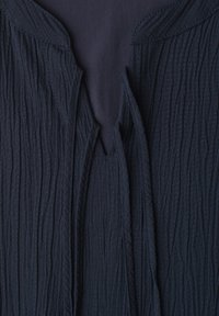 Tissu bleu marine foncé texturé avec un design froissé en couches et un décolleté ouvert sur un vêtement.