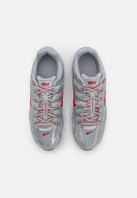 Silver athletic shoes with red accents and branding. Features mesh material and a padded tongue with laces. Designed for comfort and support.