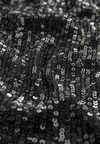 Schwarzer Stoff, verziert mit glänzenden silbernen Pailletten, die eine glatte Textur und einen subtilen Schimmer aufweisen, in einem fließenden, wellenförmigen Muster angeordnet.