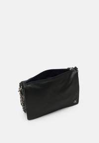Borsa a mano in pelle nera con una texture liscia, chiusura con zip e tracolla in catena argentea. Presenta un accento con il logo sul lato inferiore destro.