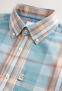 Camicia a maniche corte a quadri nei toni del verde tiffany, beige e marrone. Presenta un colletto con bottoni, taschino frontale e bottoni bianchi su un tessuto liscio.