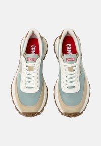 Světle modré a béžové tenisky s bílými tkaničkami, texturovaná tkanina, gumové podrážky a červený vnitřek s logem "CAMPER" na jazyku.