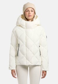 Witte gewatteerde jas met een hoge kraag en een grote capuchon, voorzien van ritszakken en een glanzende afwerking. Gecombineerd met een beige gebreide muts.