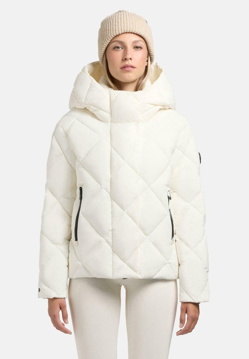 Witte gewatteerde jas met een hoge kraag en een grote capuchon, voorzien van ritszakken en een glanzende afwerking. Gecombineerd met een beige gebreide muts.