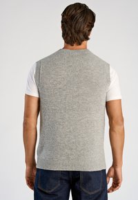 Grå stickad väst med rund halsringning och ribbad kant, bärs över en vit skjorta. Har en texturerad yta och är ärmlös.