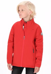 Rød softshell-jakke med høj krave, lynlås og logo-patch på ærmet. Har en glat tekstur og tætsiddende design.