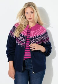 Cardigan blu navy con cerniera, decorato con un motivo geometrico rosa e bianco, collo e polsini a coste, indossato sopra una camicia a righe rosa e bianche.