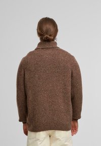 Brauner gestrickter Pullover mit hohem Kragen, strukturierter Oberfläche und gerippten Bündchen. Lockere Passform in solider Farbe mit subtilem gesprenkeltem Muster.