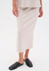 Hame midi vaaleanbeigeä sileästä kankaasta, suoralinjainen siluetti ja sivuaukko, yhdistettynä mustiin liukuhyppymommoihin.