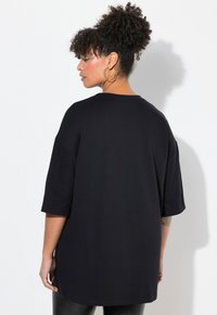 T-shirt noir surdimensionné à manches courtes, col rond et tissu doux. Montre un dos lisse sans motifs ni embellissements visibles.