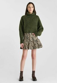 Groen donzig cropped sweater met col, gecombineerd met een gerimpelde mini-jurk met leopardprint. Bruine sokken en zwarte schoenen maken de outfit compleet.