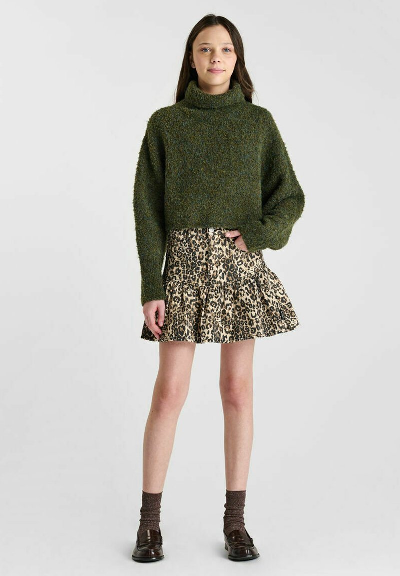Groen donzig cropped sweater met col, gecombineerd met een gerimpelde mini-jurk met leopardprint. Bruine sokken en zwarte schoenen maken de outfit compleet.