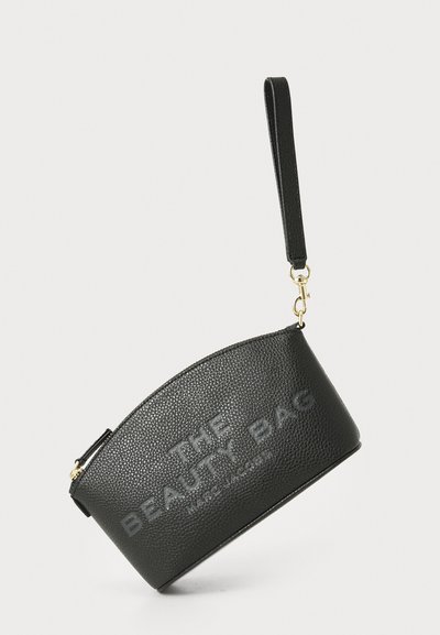 Čierna kožená kozmetická taška s textúrovaným povrchom, vybavená embosovaným textom "THE BEAUTY BAG", odnímateľným popruhom a zlatými kovovými detailmi.