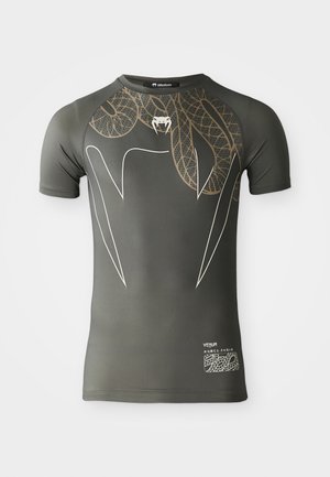 Dark green fitted athletic shirt with short sleeves, featuring a large brown leaf pattern, sharp white lines, and a small white logo near the hem.