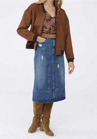 Femme portant une veste en daim marron, un top à motifs, une jupe midi en jean délavé avec ceinture, et des bottes hautes en daim beige.