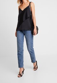 Svart satin camisole med draperad framsida, tillsammans med ljusblå raka jeans och svarta remsandaler med hög klack.