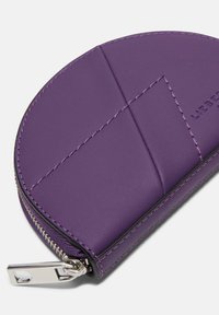 Lila Ledertasche in runder Form, mit genähten Akzenten, einem Reißverschluss und einem silbernen Zugknopf. Minimalistisches Design mit Kartenfächern.