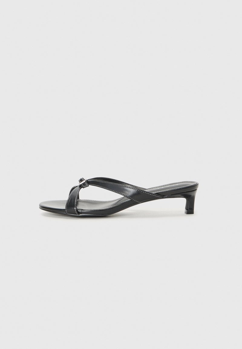 Sandales noires à talons avec un design à lanières croisées en matériau synthétique lisse. Présentent un talon carré bas et un accent décoratif à la jonction des lanières.