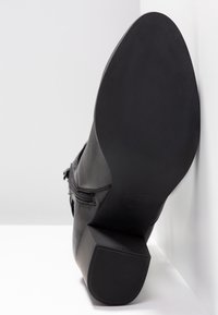 Botte noire en cuir avec une surface texturée, un talon carré et une fermeture éclair. La semelle est lisse avec un motif de bande de roulement subtil.