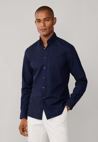 Camicia blu navy con bottoni, realizzata in tessuto di cotone liscio. Presenta maniche lunghe, colletto classico e bottoni abbinati. Design semplice e versatile.