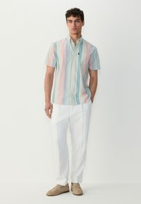 Koszula z krótkim rękawem na guziki w pastelowy paskowany wzór w zielonym, różowym i niebieskim kolorze, zestawiona z dopasowanymi białymi spodniami i beżowymi mokasynami.