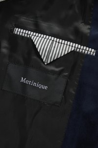 Melnas satīna jakas oderējums ar svītrainu auduma cilpu un aizšūtu etiķeti ar uzrakstu "Matinique" uz tumši zila auduma.