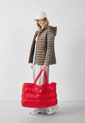 Bruine pufferjack met capuchon en ritssluiting, gecombineerd met een grote, puffy rode tas met korte handvatten en een logopatch.