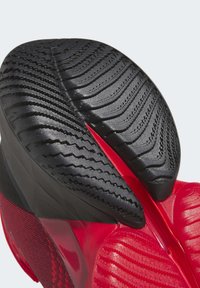 Suela de zapatilla deportiva roja con una suela de goma negra texturizada, que presenta patrones en zigzag para tracción y un detalle superior rojo liso.