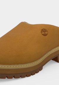Κοντινή λήψη καφέ παπουτσιού τύπου slip-on με υφή στην σόλα και ραμμένη επένδυση, με μικρό λογότυπο δέντρου στο πάνω μέρος.