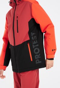 Rote und schwarze Skijacke mit durchgehendem Reißverschluss, Logodruck und Kontrastakzenten. Verfügt über Reißverschlusstaschen und verstellbare Bündchen.