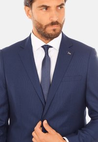 Abito blu navy con texture sottile, design a un petto, rever a punta e vestibilità slim. Accentuato con una cravatta e una spilla per rever.