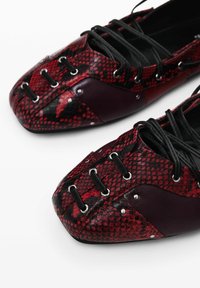 Rood en zwart slangprint schoenen met een spitse neus, voorzien van zwarte veters, metalen oogjes en leren accenten. Ge textured glanzende afwerking.