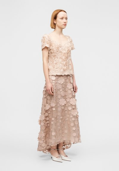 Φλοράλ φόρεμα δύο τεμαχίων σε ανοιχτό μπεζ. Το τοπ έχει υφασμένα εφαρμοστά τριαντάφυλλα· η φούστα διακοσμημένη με κοψίματα σε σχήμα λουλουδιών και διαφανή στρώματα.