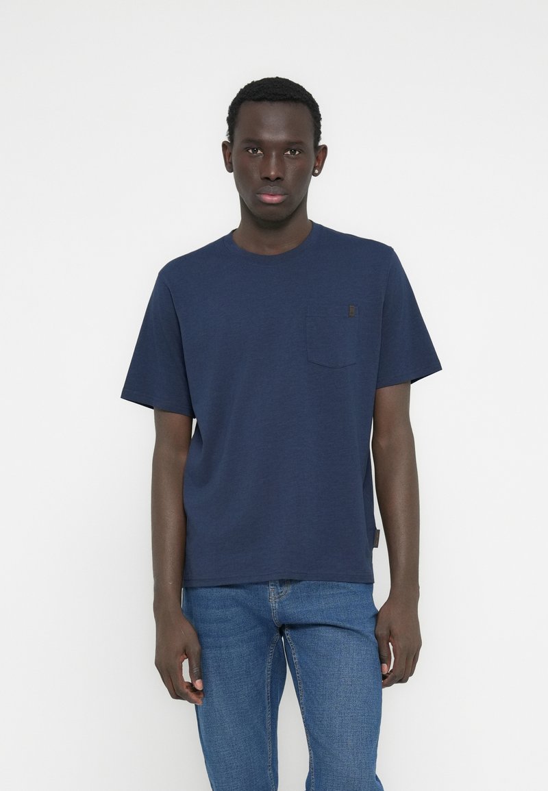 Μπλε ναυτικό βαμβακερό μπλουζάκι με στρογγυλή λαιμόκοψη, κοντά μανίκια και τσέπη στο στήθος. Διαθέτει μια μικρή ετικέτα μάρκας στη ραφή πλευράς.