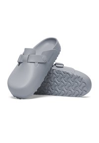Zoccoli grigi in gomma liscia, con una fascia decorativa e suola testurizzata e modellata per una migliore presa. Leggeri e facili da pulire.