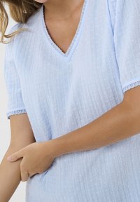 Blusa corta de manga corta de color azul claro con escote en V, que presenta puntos texturizados y un delicado borde de encaje a lo largo del escote y las mangas.