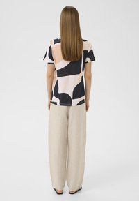 Top cu mâneci scurte în roz pastel, decorat cu modele abstracte mari în negru și bej. Asortat cu pantaloni din in ușori, lejeri, de culoare bej deschis.