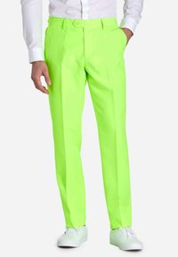 Neon-grüne Hose mit tailliertem Schnitt, mit vorderen Falten und Seitentaschen, kombiniert mit weißen Sneakers und einem weißen Hemd mit Knöpfen.